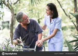 Nurse with patient using walker in retirement home. Young female nurse holding old man's hand in outdoor garden walking. Senior care, care taker and senior retirement home service concept.